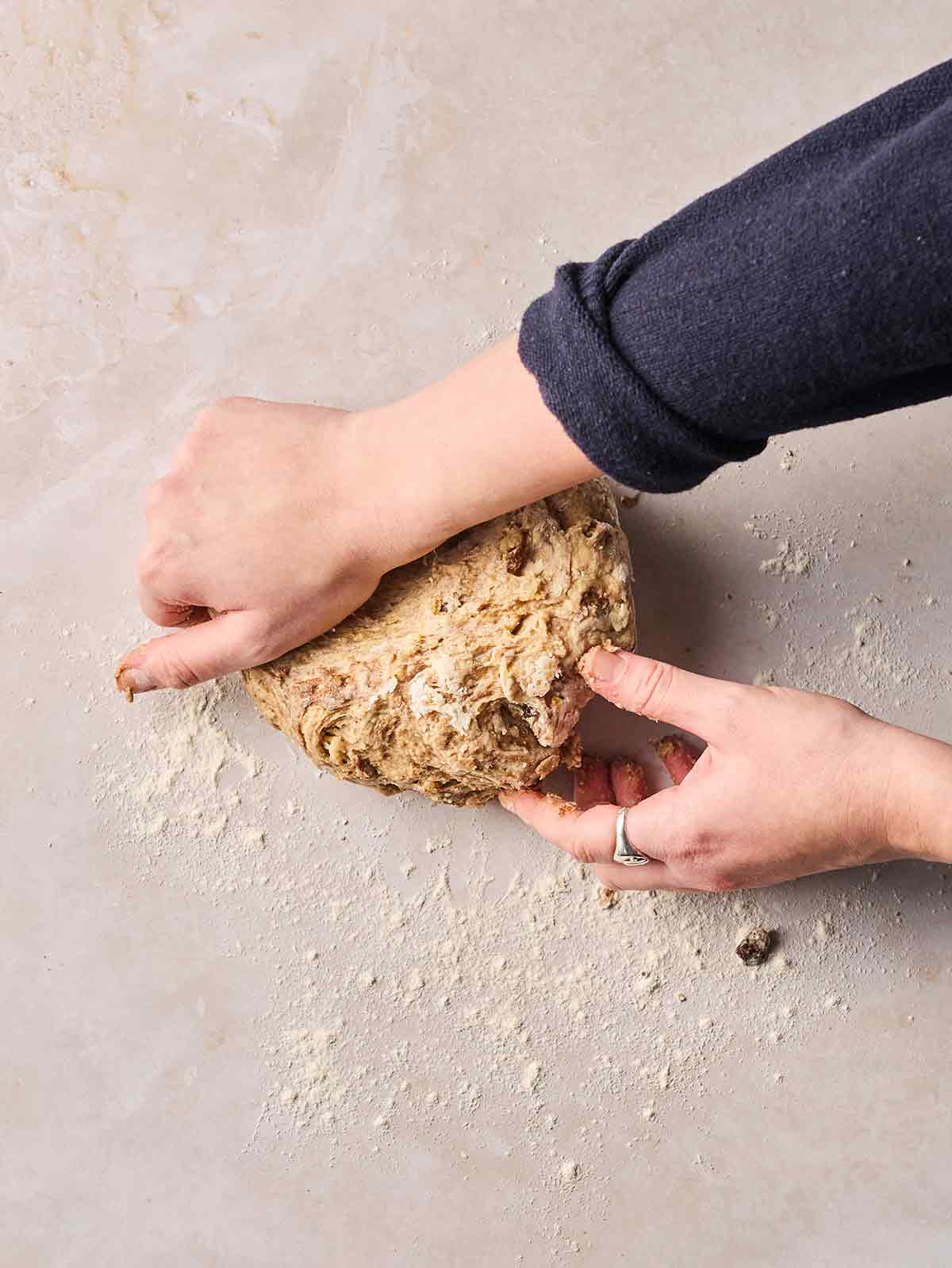 Two hands kneading dough for Hot Cross Buns on a white surface.