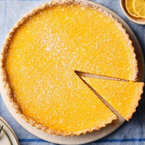 A lemon tart with a slice missing, ready to eat, on a table.
