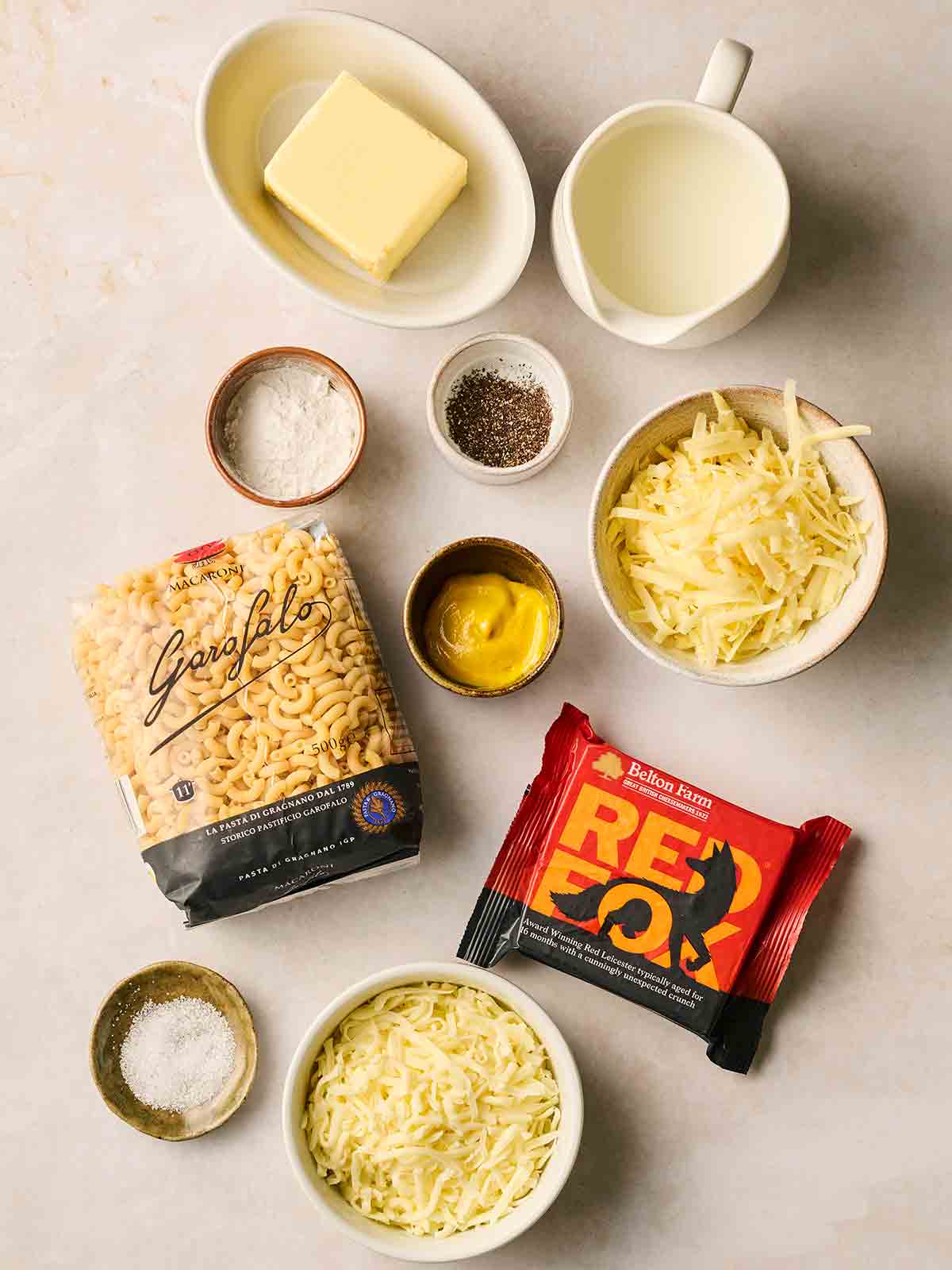The ingredients for making homemade Macaroni Cheese laid out on a white surface.