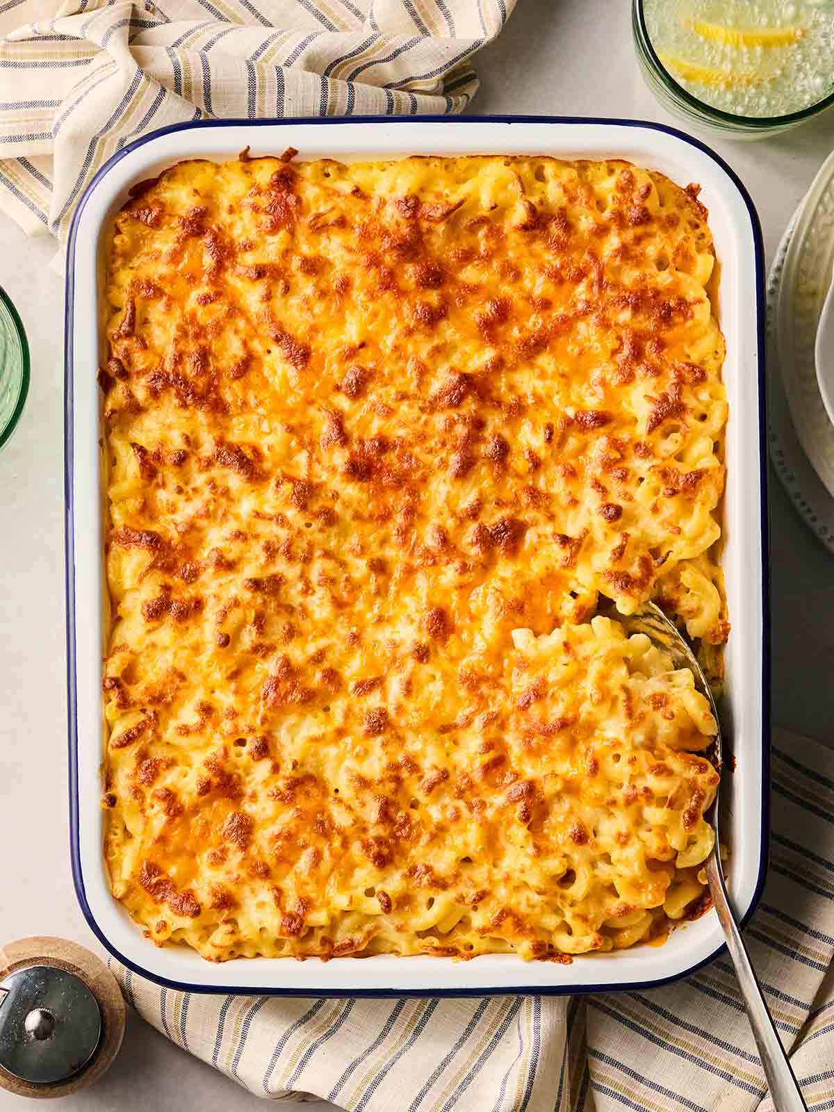 An oven dish with golden baked Macaroni Cheese, with a spoon ready to serve.