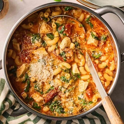 A bowl of tomatoey chicken pasta soup on a table, ready to serve.