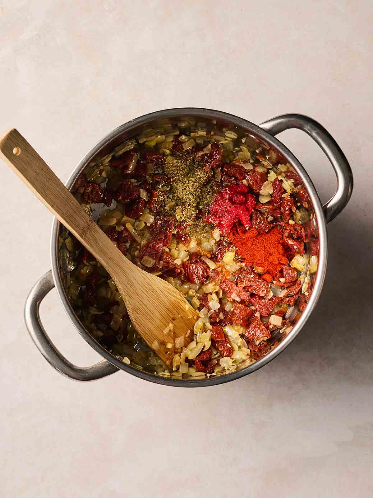A pan with frying ingredients inside, including sun-dried tomatoes, onion and herbs and spices.