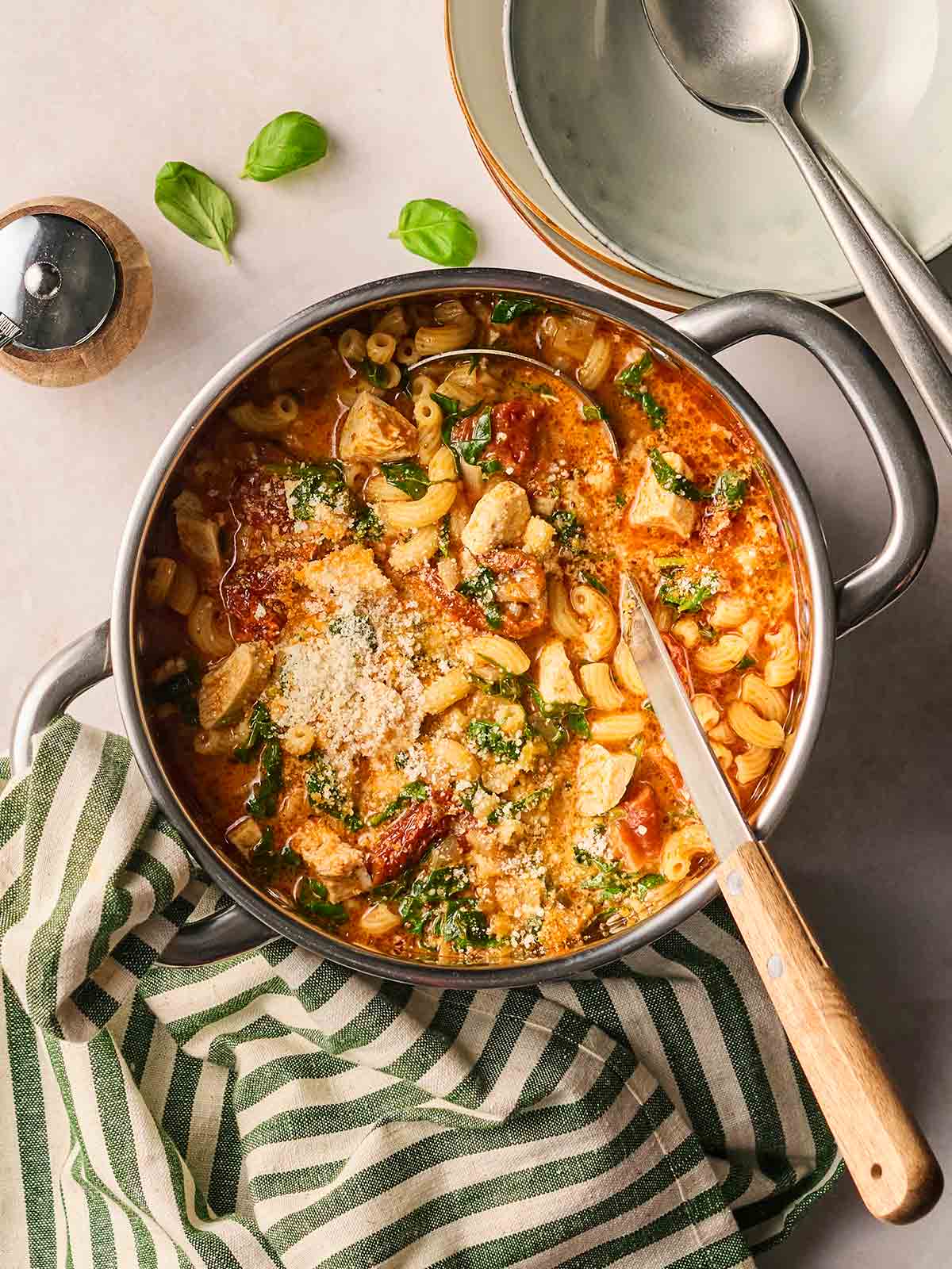 A pan filled with Marry Me Chicken Soup on a table with a tablecloth to the side, a ladle in to serve, and bowls to the side.