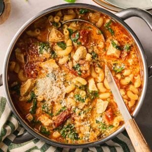 A pan filled with tomatoey soup with chicken, spinach, parmesan and cream with a ladle in, ready to serve.
