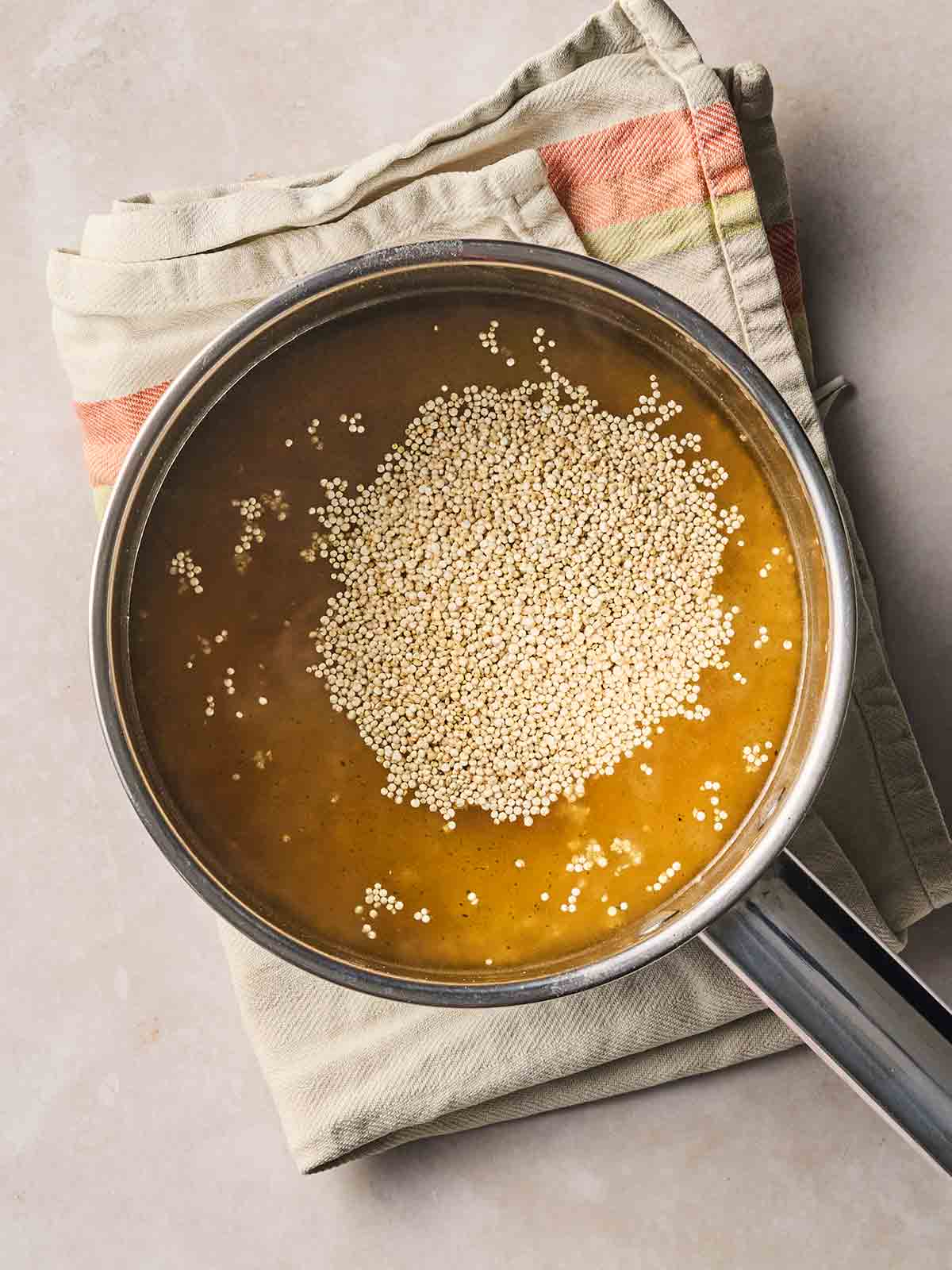 Quinoa in a pan of water on a white surface with a tea towel underneath.