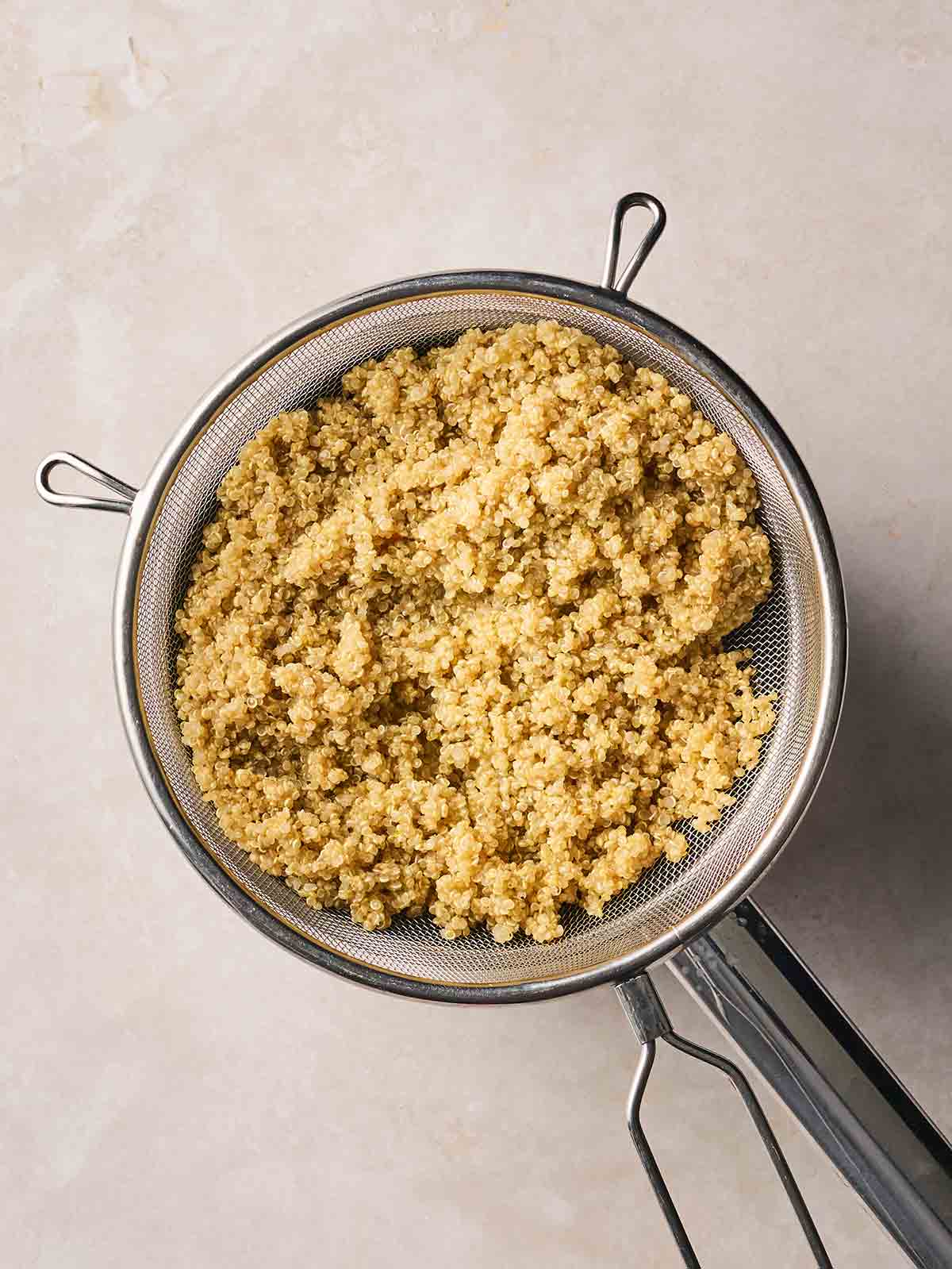 A sieve full of drained cooked quinoa over a pan on a white surface.