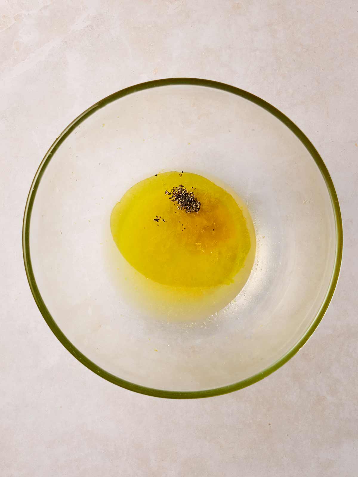 A glass bowl filled with oil, lemon zest and salt and pepper, ready to be served, for a salad dressing.