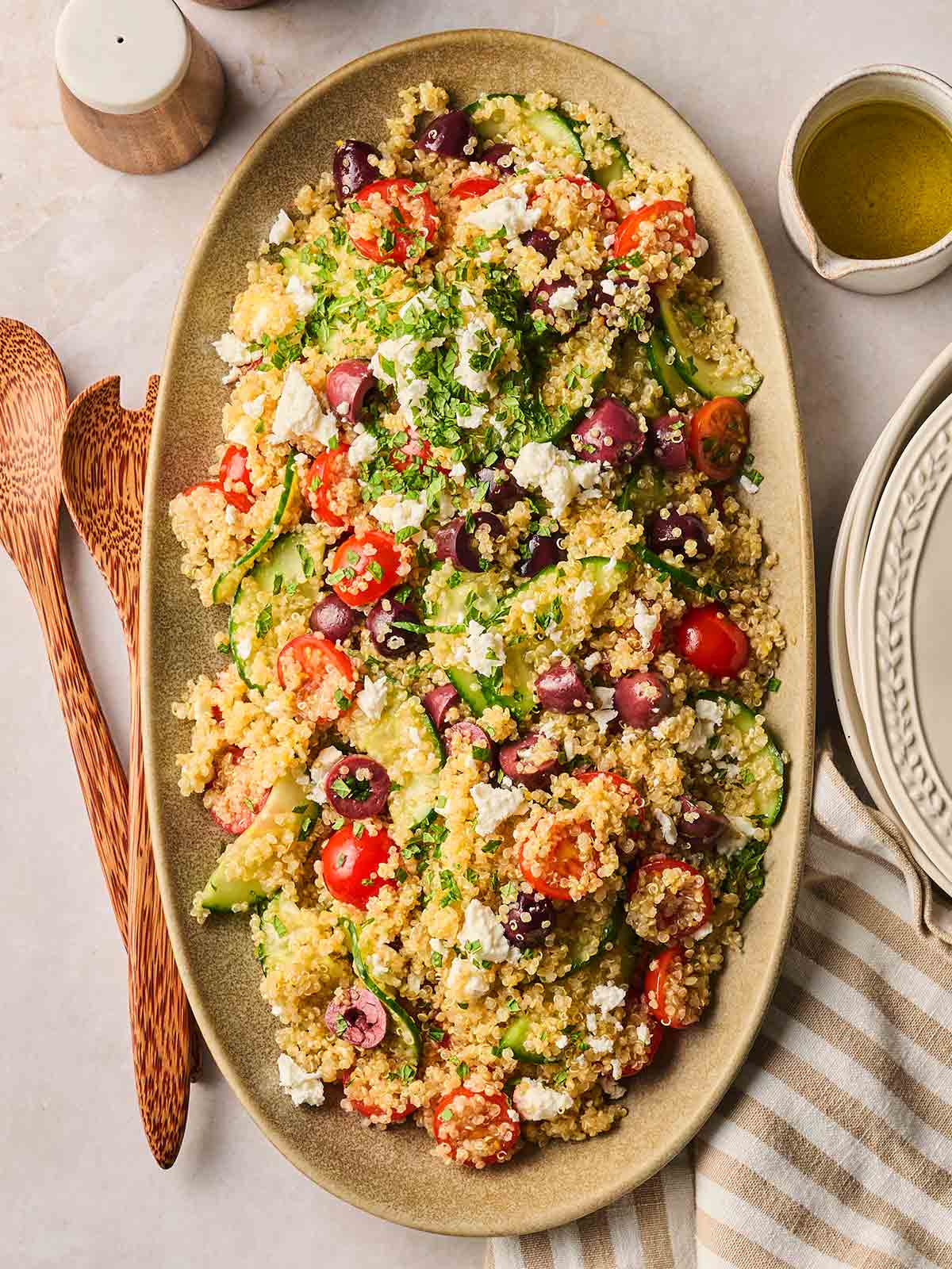 A platter with a quinoa salad on, ready to be served on plates on a table, with wooden utensils at the side.