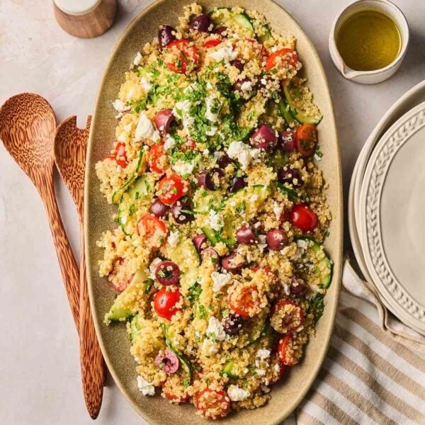 A platter on a dining table with quinoa, tomato, cucumber, olives and feta.