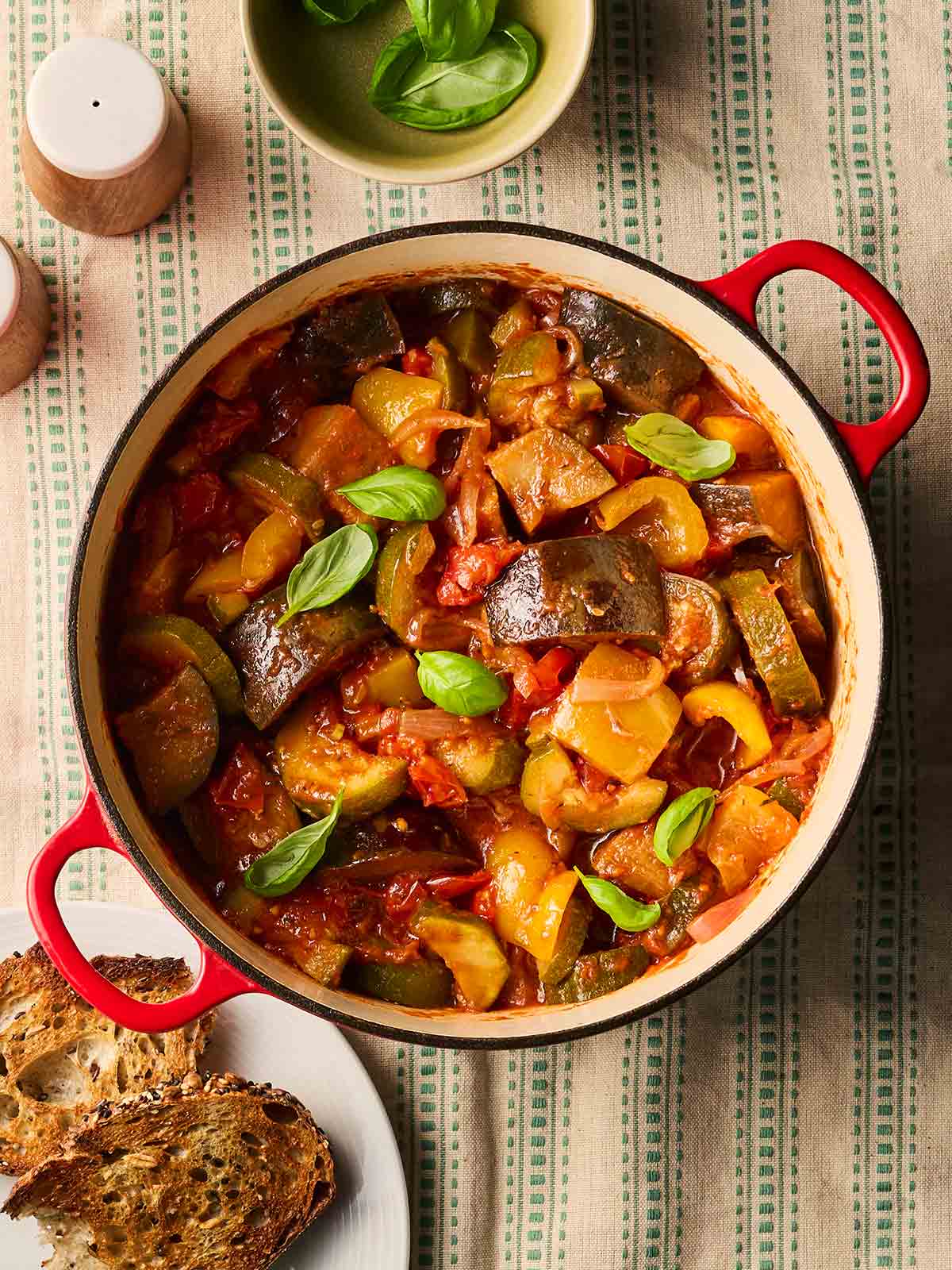 A pan of Ratatouille on a table, ready to eat, with lots of vegetables and a tomato sauce.