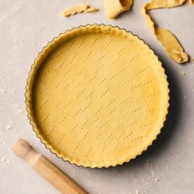 A close up of unbaked shortcrust pastry in a flan dish, ready to bake.
