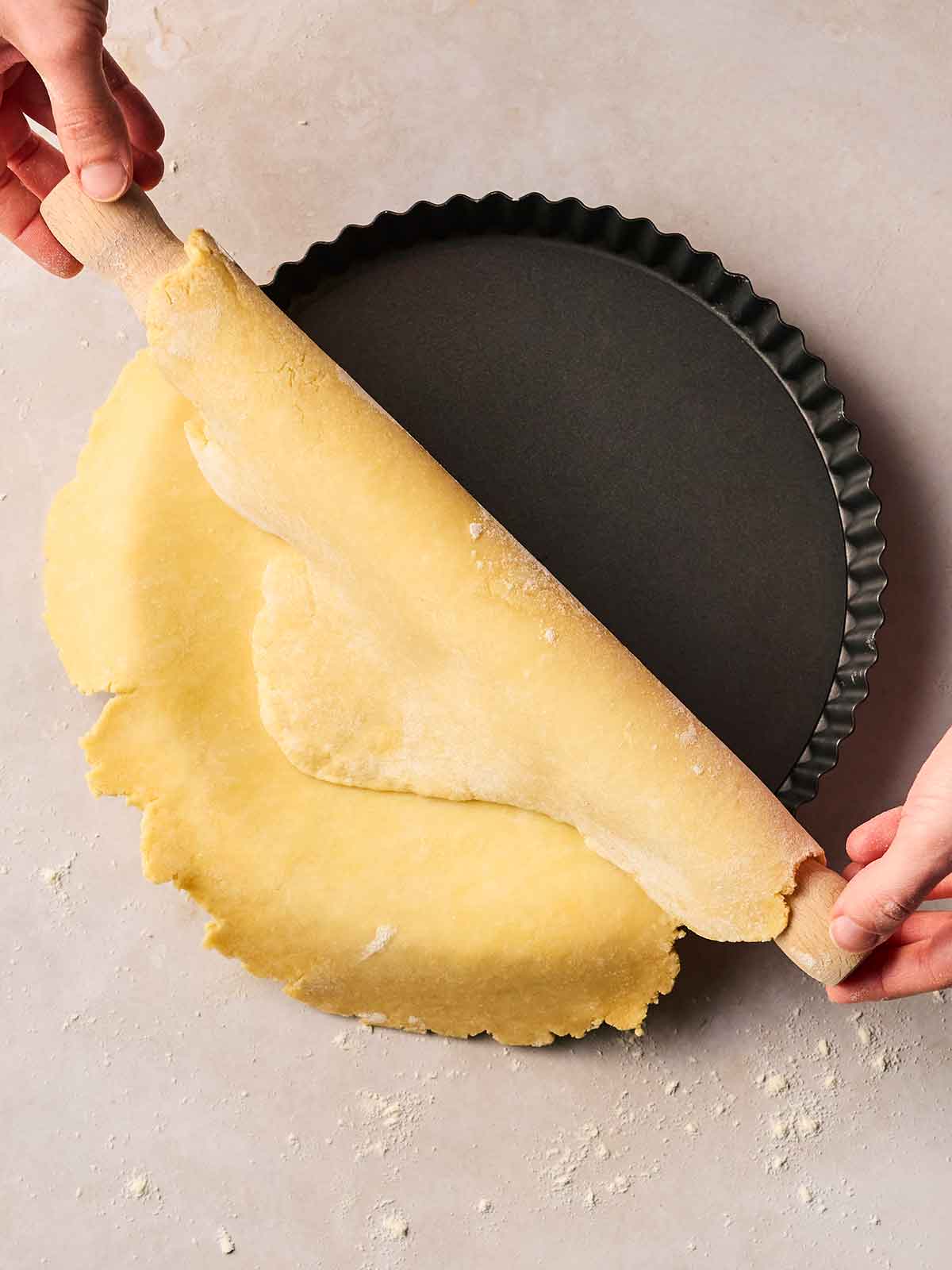 A flan dish with two hands rolling over homemade pie crust into it.