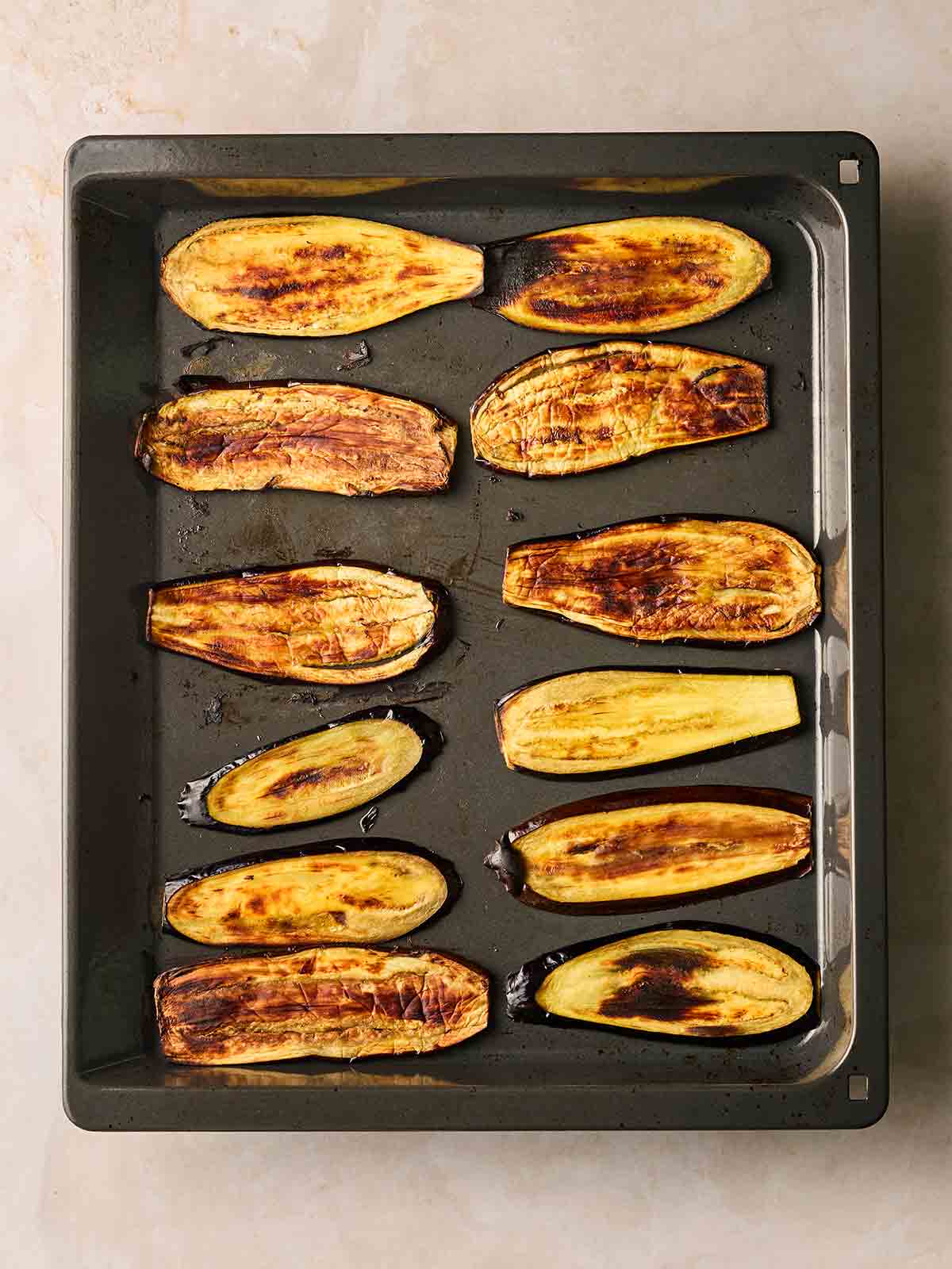 A baking sheet on a white surface, with grilled golden aubergine slices in.