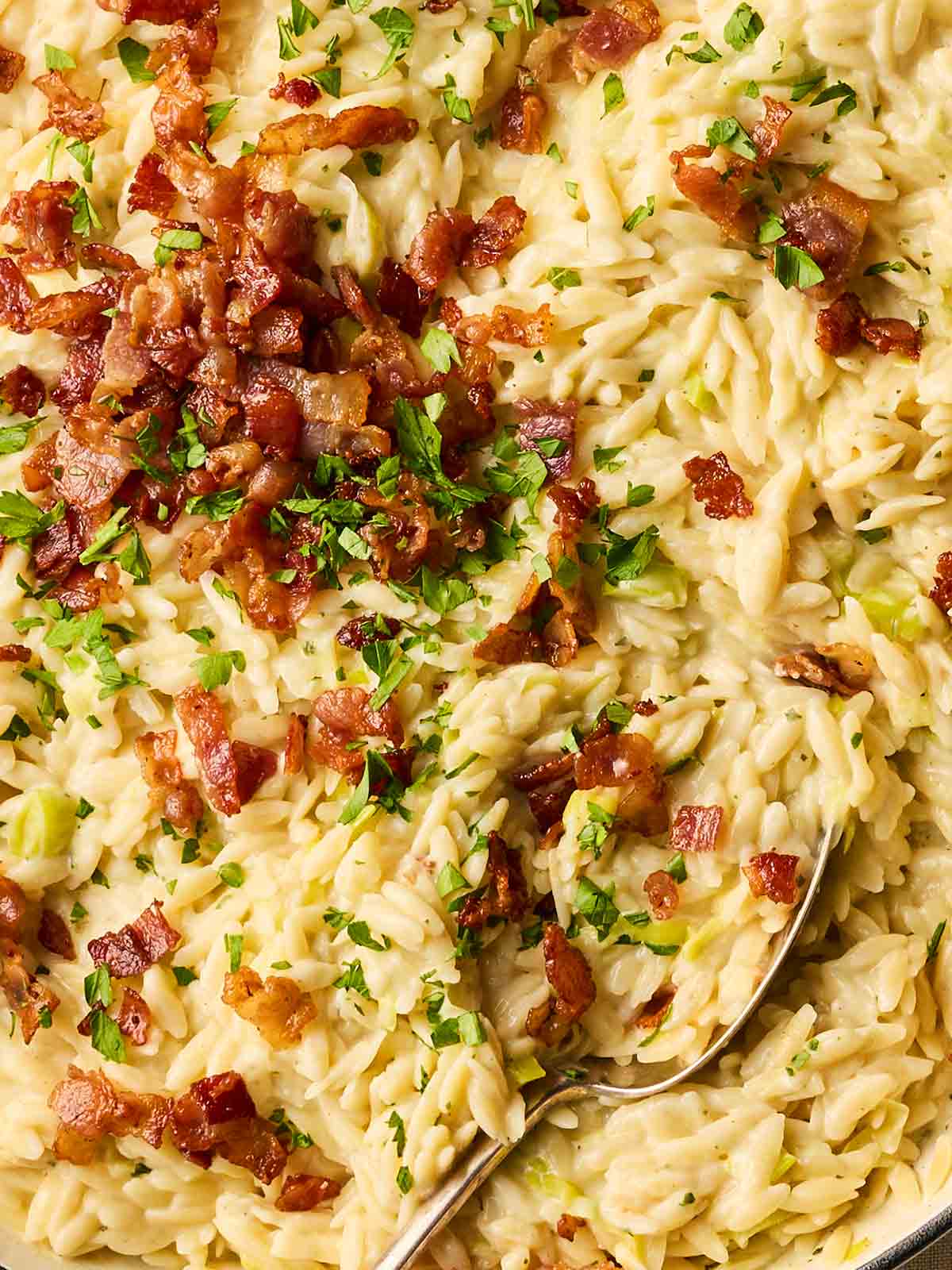 A close up of a one pot dish, with orzo, bacon and leeks all mixed together.