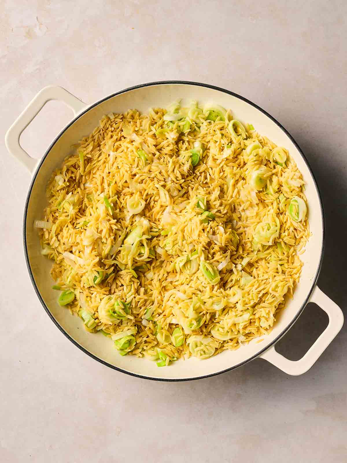 A pan with dried orzo and leeks in a pan for step 2 in the recipe for a one pot pasta.