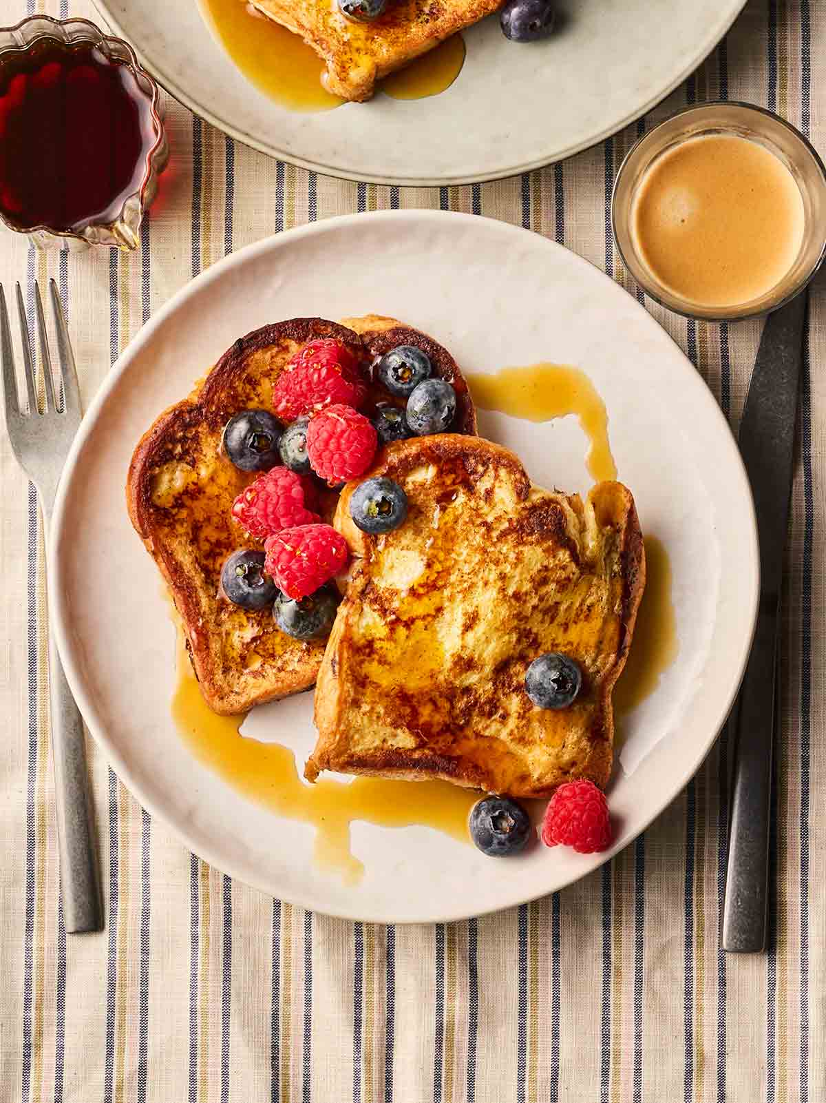 A plate of two slices of French Toast, with maple syrup and berries on top, at a set table, ready to eat.