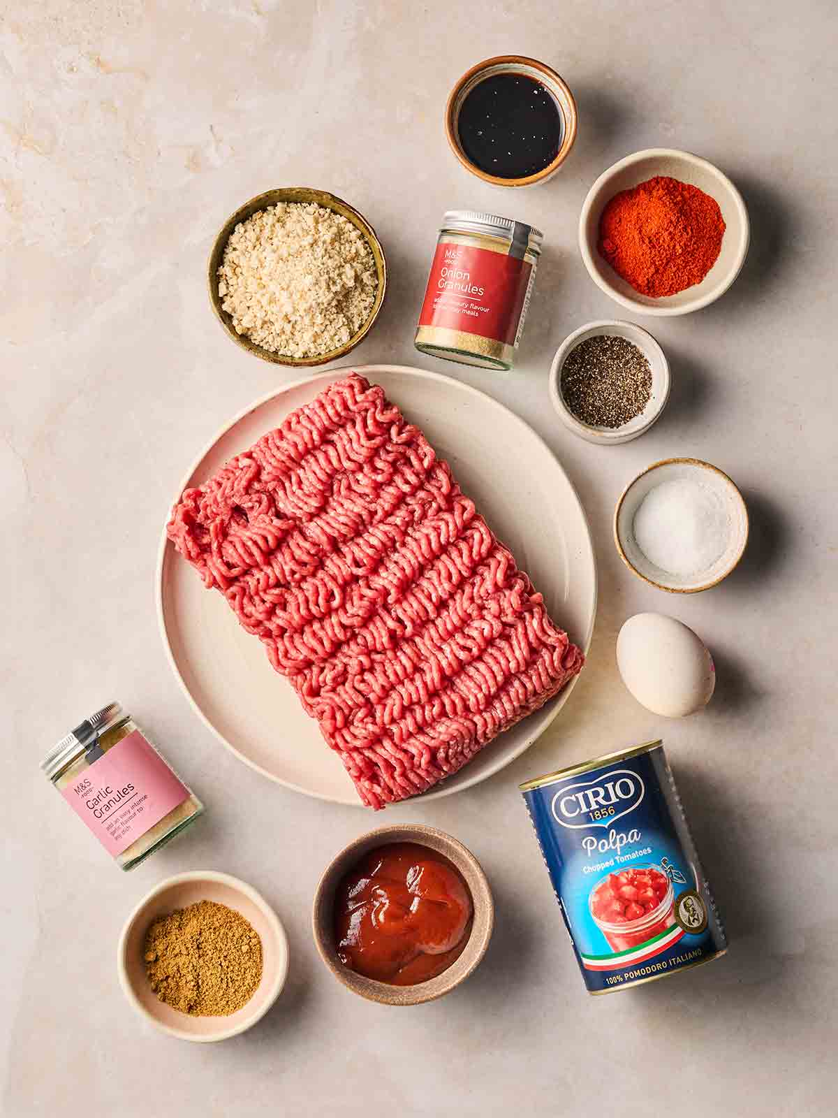 The ingredients for making a homemade meatloaf in bowls and plates on a white surface.
