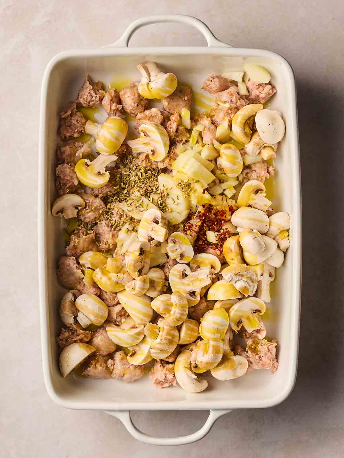 Chopped, raw ingredients in an oven dish with oil drizzled for a Sausage Orzo bake dish.