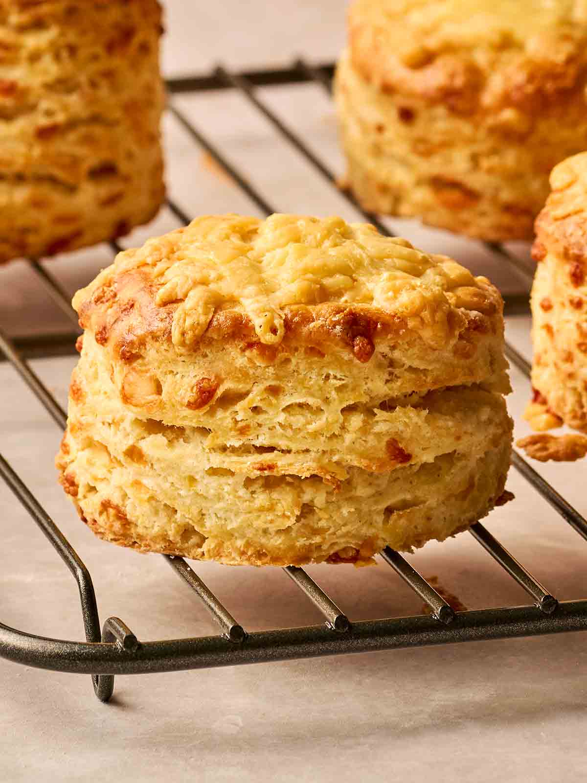 A side view of a cheese scone on a wire rack, with others in the background, just baked.