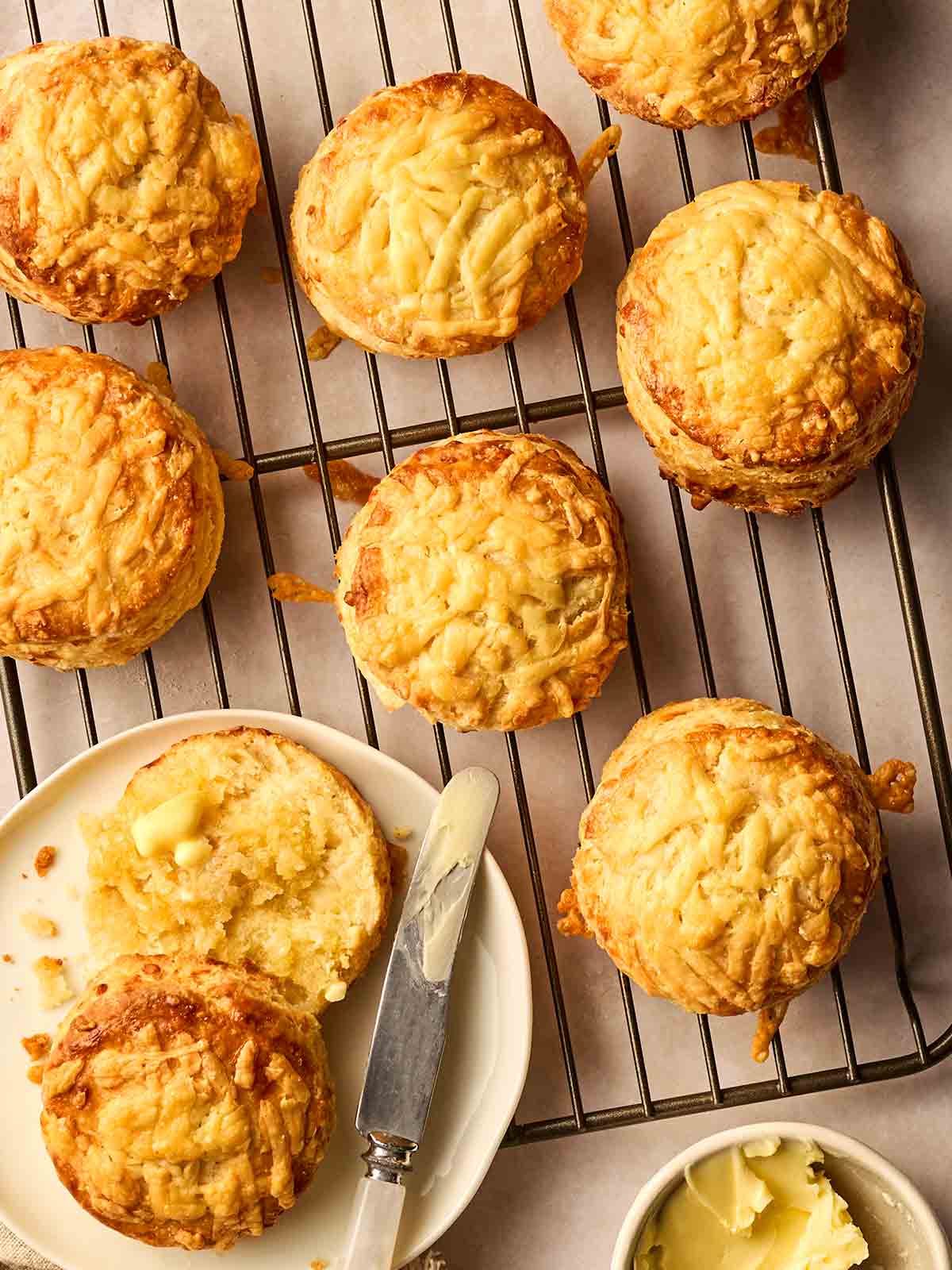 Baked Cheese Scones on a wire rack with a side plate and knife, with one scone buttered.