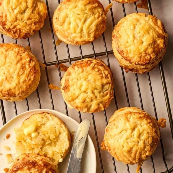 A round wire rack with baked Cheese Scones on and one buttered on a plate.