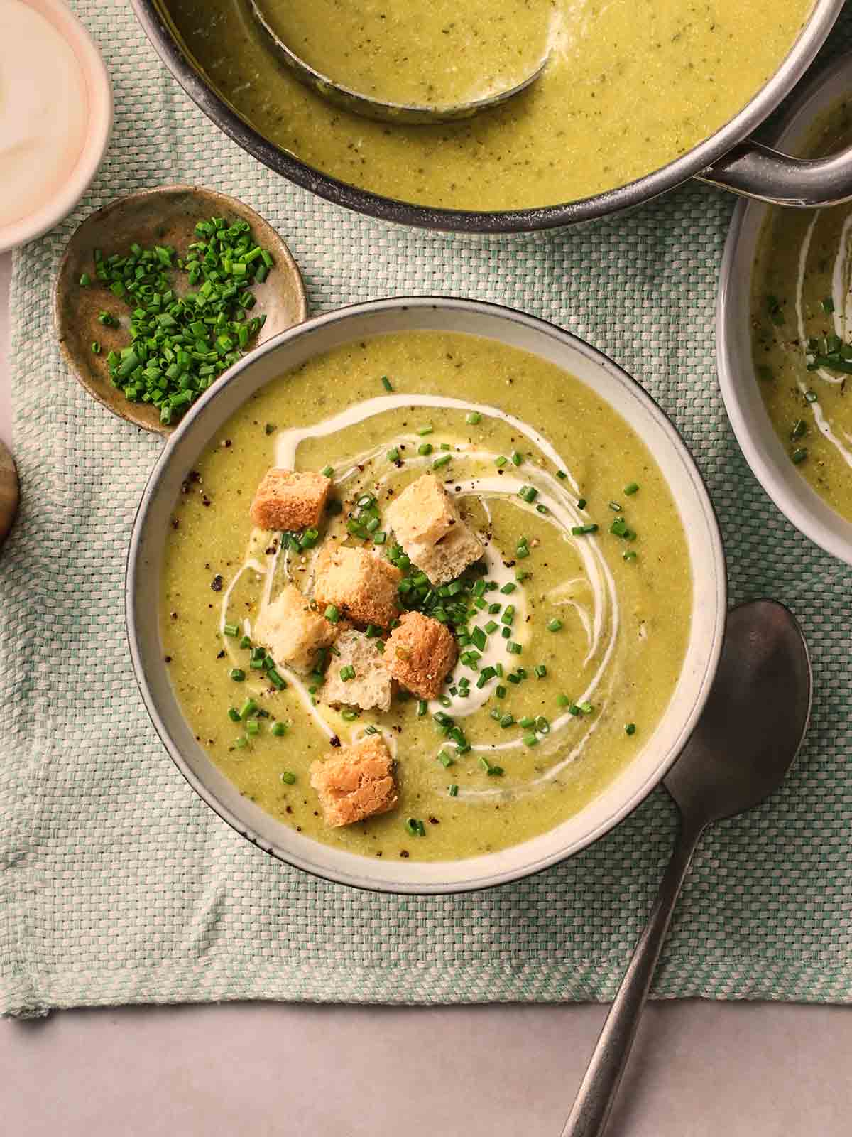 A green soup on a table, having been served into a plate with croutons.