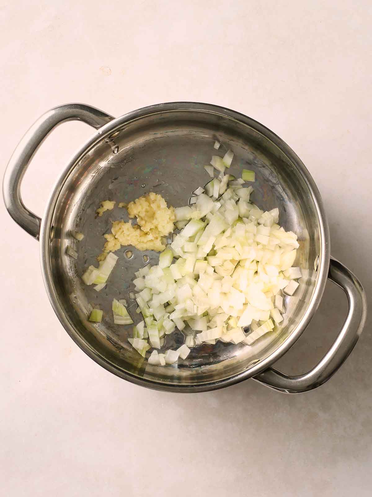 A metal pan on a white surface with sauteed onion and garlic in.