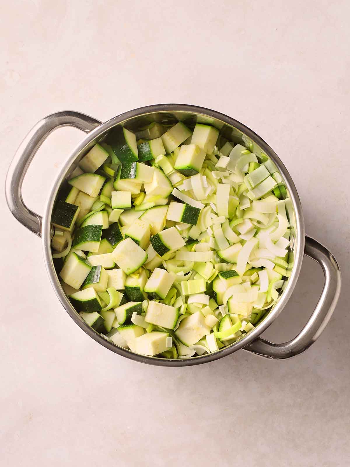 Raw vegetables including courgettes and leeks in a metal pan on a white surface.