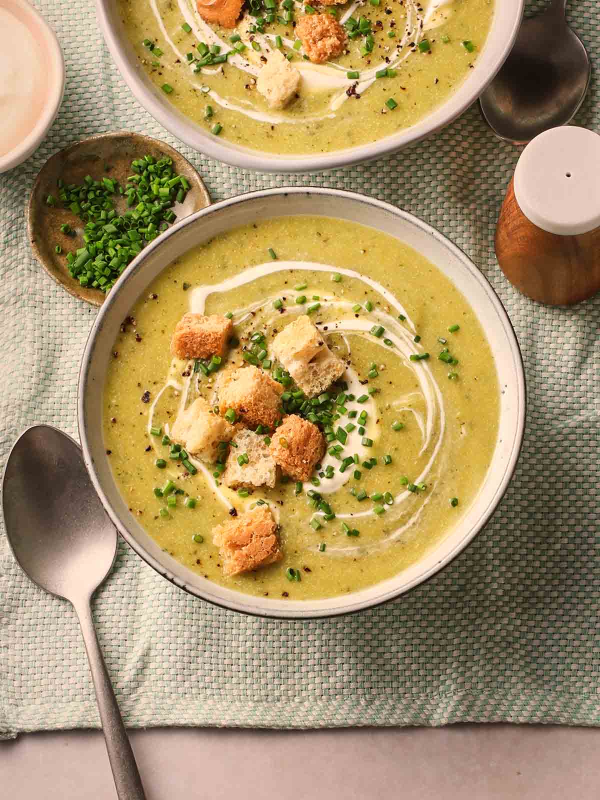 A set table with two bowls of courgette soup with croutons, ready to eat.