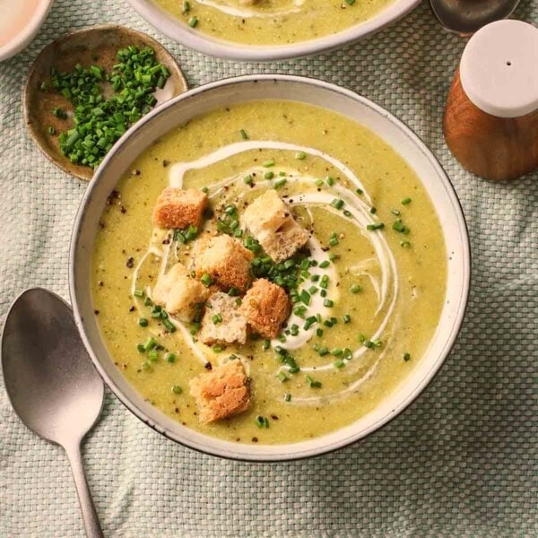 A close up of a bowl of courgette soup with croutons and chives, ready to eat on a set table.
