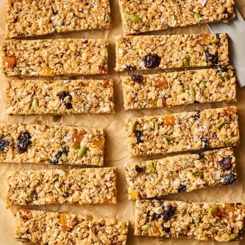 Homemade breakfast bars made with oats, rice crispy cereal and dried fruit, on a baking paper sheet with a knife to the side.