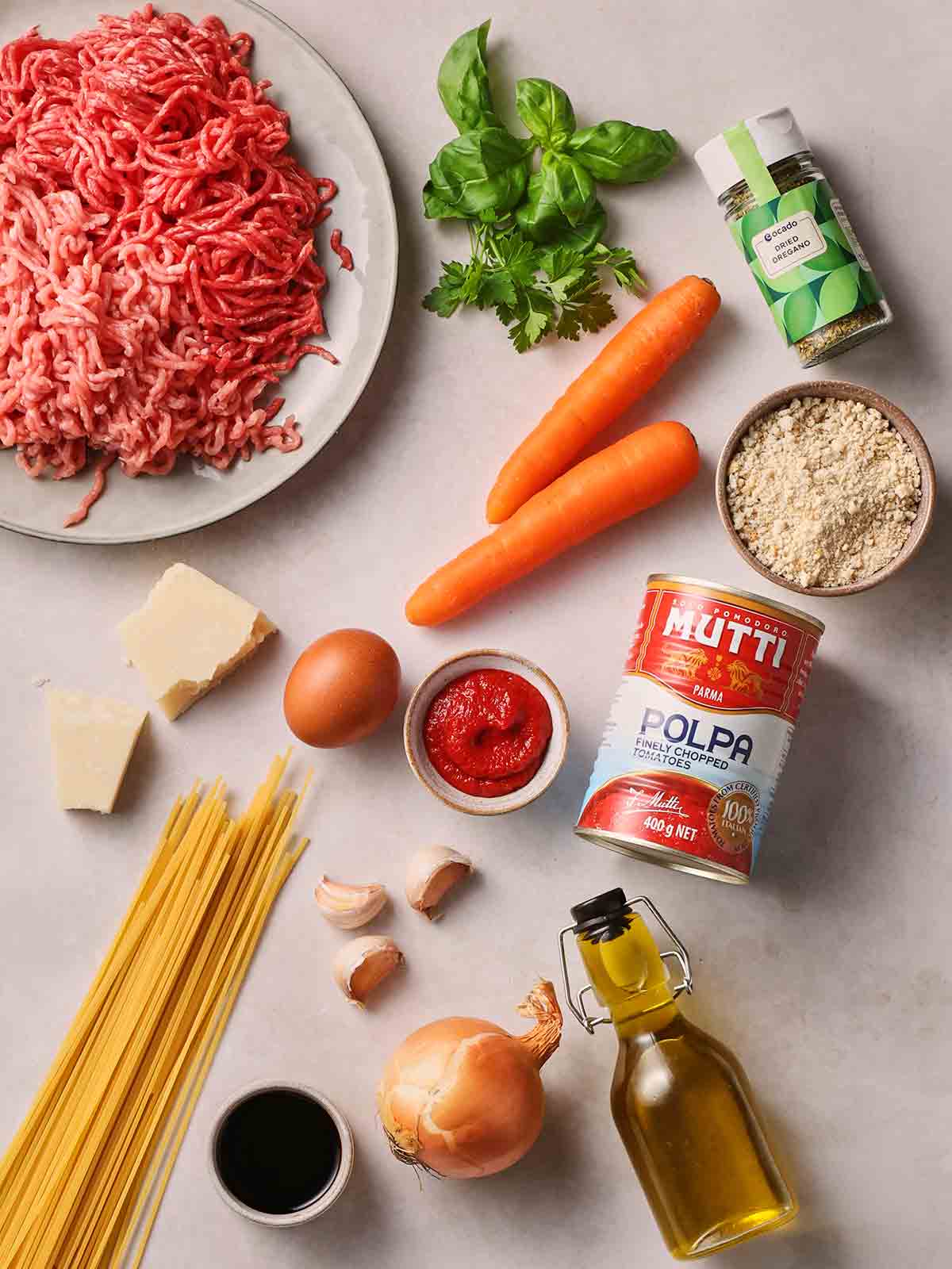 The raw ingredients for making classic meatballs laid out on a white surface.