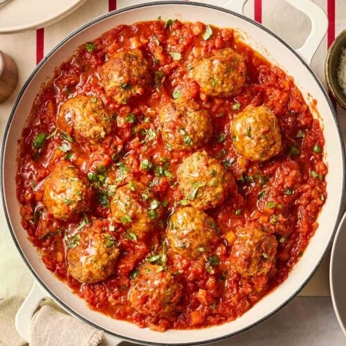 A pan filled with meatballs in a classic Italian tomato sauce, in the middle of a table, ready to serve up onto plates.