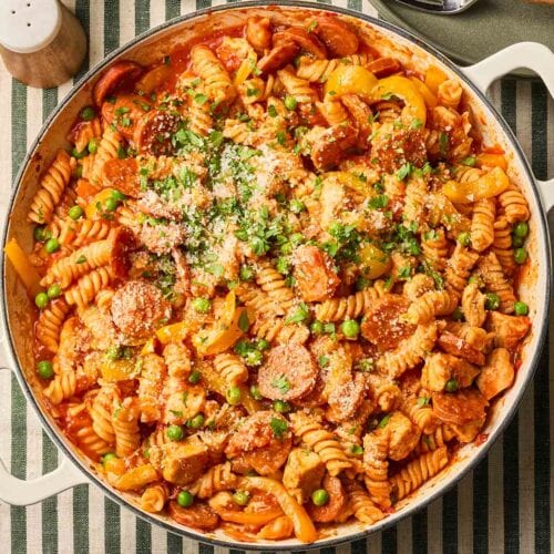 A pan of chicken and chorizo pasta about to the served, sitting on a green and white stripy tablecloth.