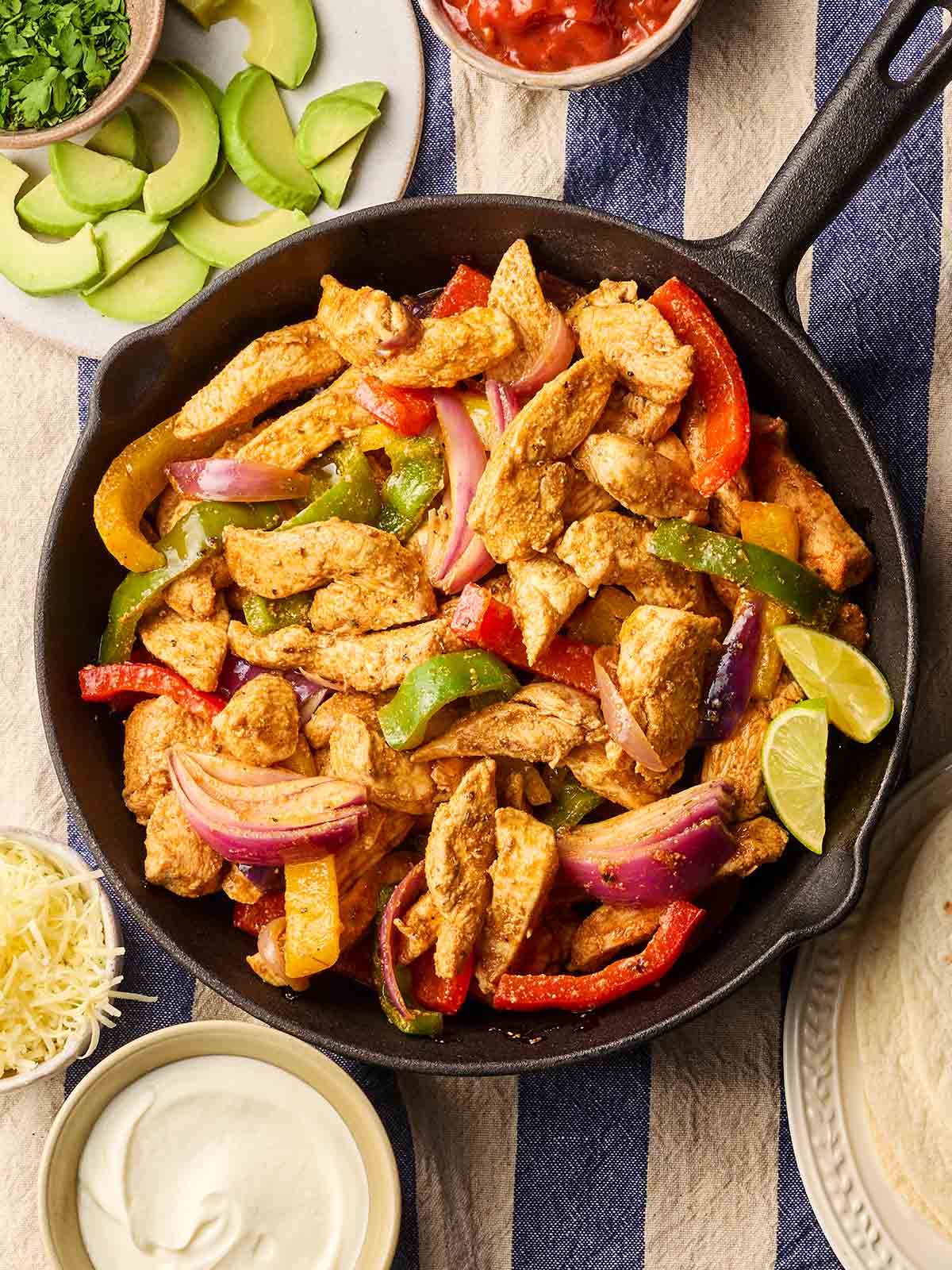 A pan on a set dinner table, filled with cooked fajitas, ready to serve up with side dishes.