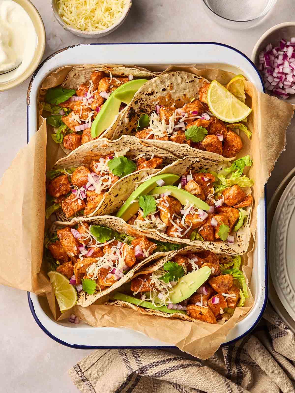 An oven dish with chicken tacos inside, with lots of toppings around the sides, ready to serve.