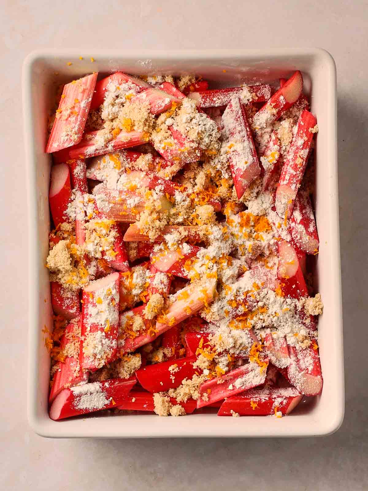An ovenproof dish on a white surface, with the filling ingredients inside for a rhubarb crumble.