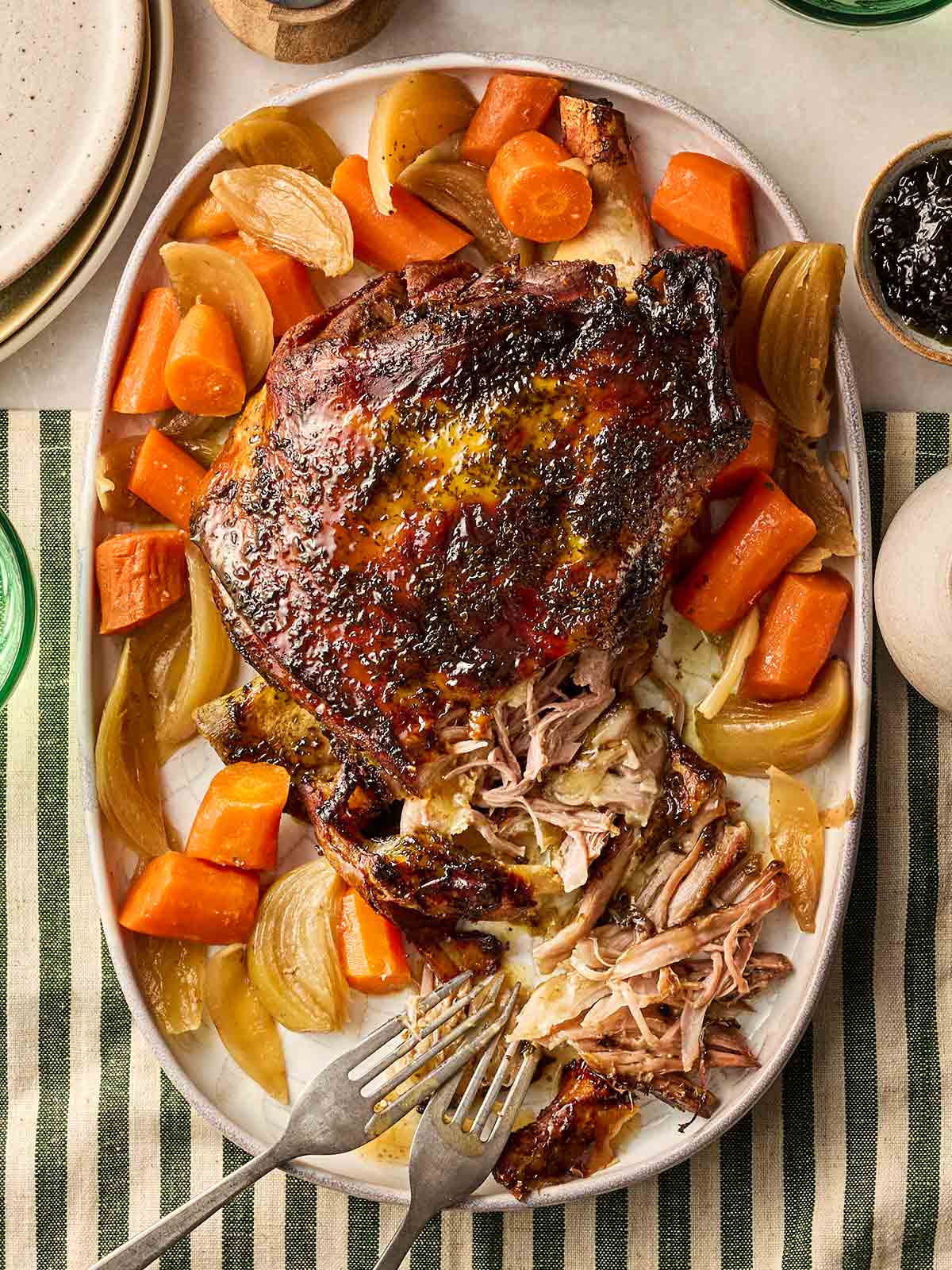 A slow cooker lamb shoulder joint with carrots and onion on a platter, on dining table, ready to be served.