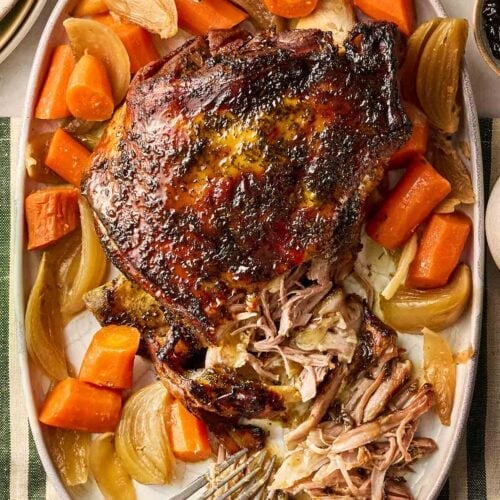 A slow cooked lamb shoulder shredded with two forks on one side, with carrots and onions, ready to eat.