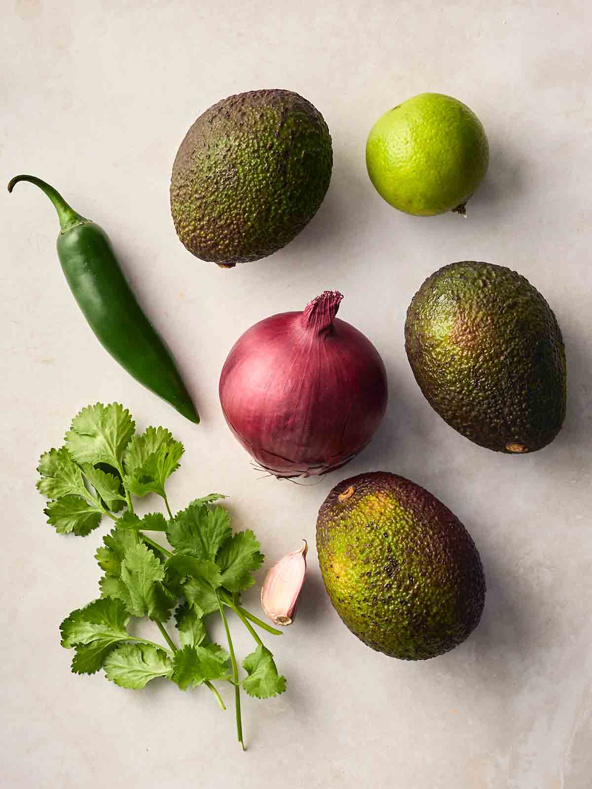The ingredients for making homemade guacamole laid out on a white surface.