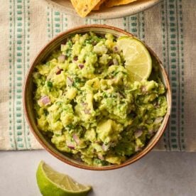 A bowl of homemade guacamole on a table with limes round the side.