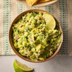 A bowl of homemade guacamole on a table with limes round the side.