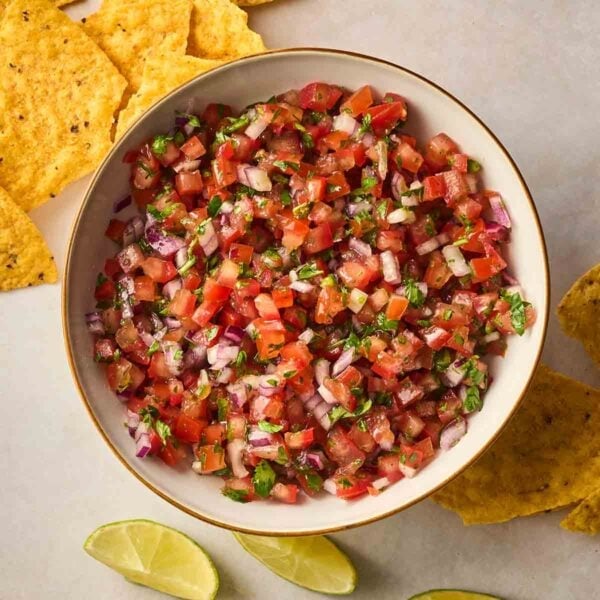 A bowl filled with fresh Salsa, with tortilla chips and lime wedges on the surface to the side.