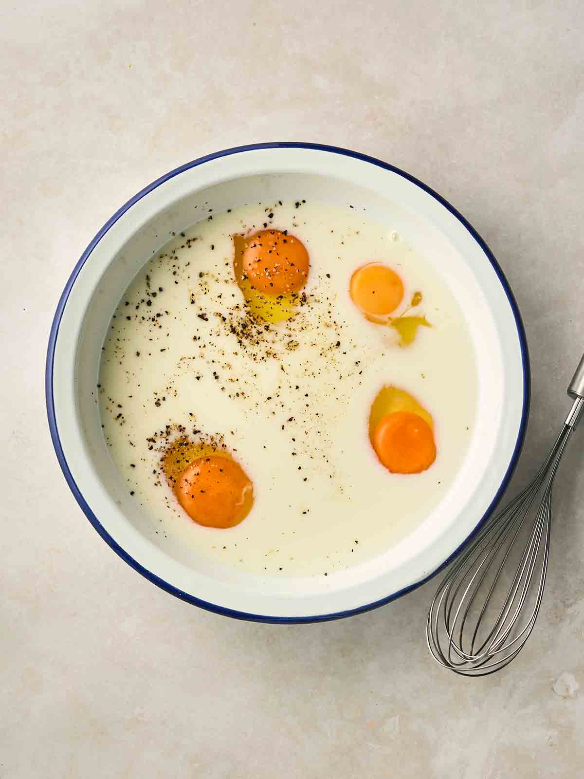 Four eggs in a wide bowl with milk and salt and pepper.